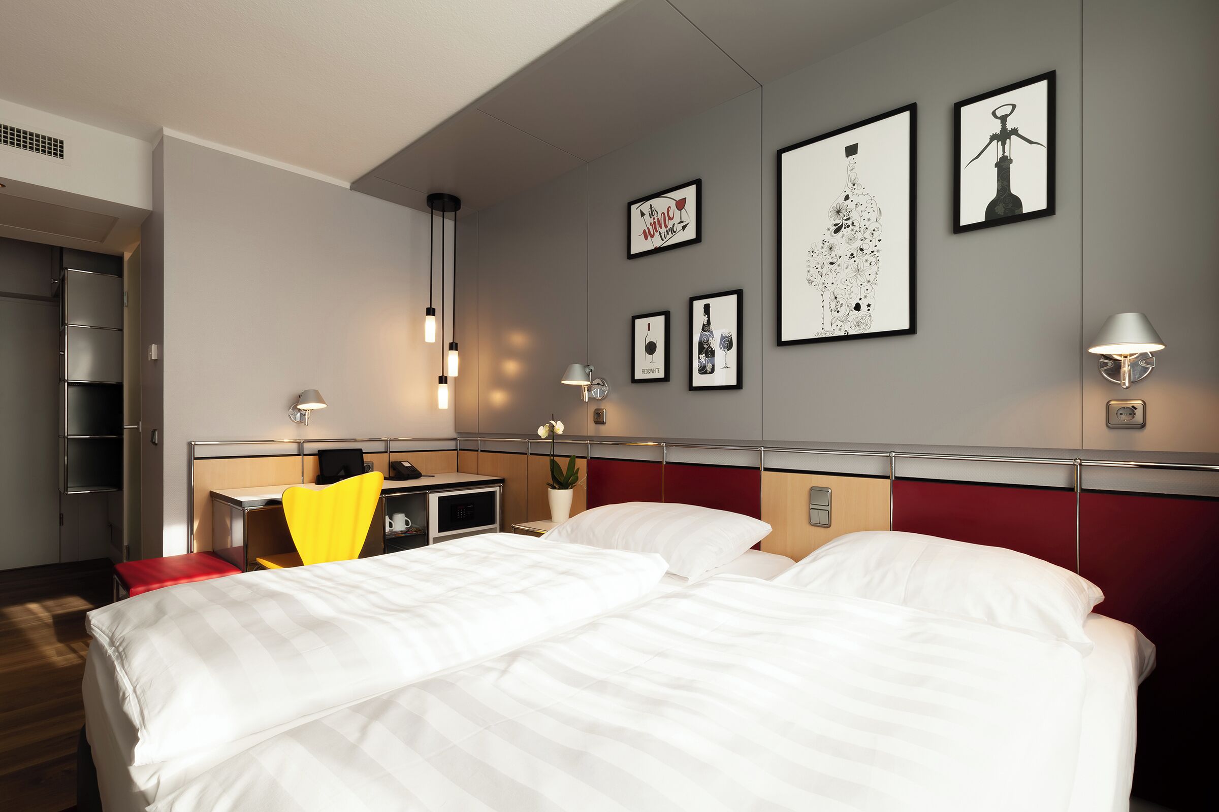 A hotel room with a bed, a desk, a chair, and artwork on the walls.