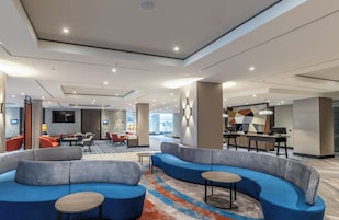 Un moderno vestíbulo de hotel con un sofá azul curvo, un comedor y un bar.