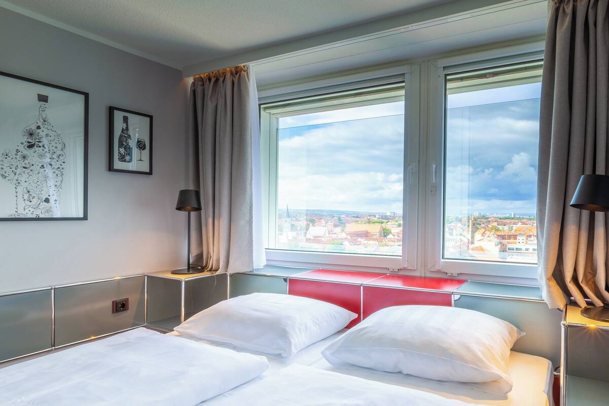 Una habitación de hotel con una cama, una mesita de noche, una lámpara y una ventana con vista a la ciudad.