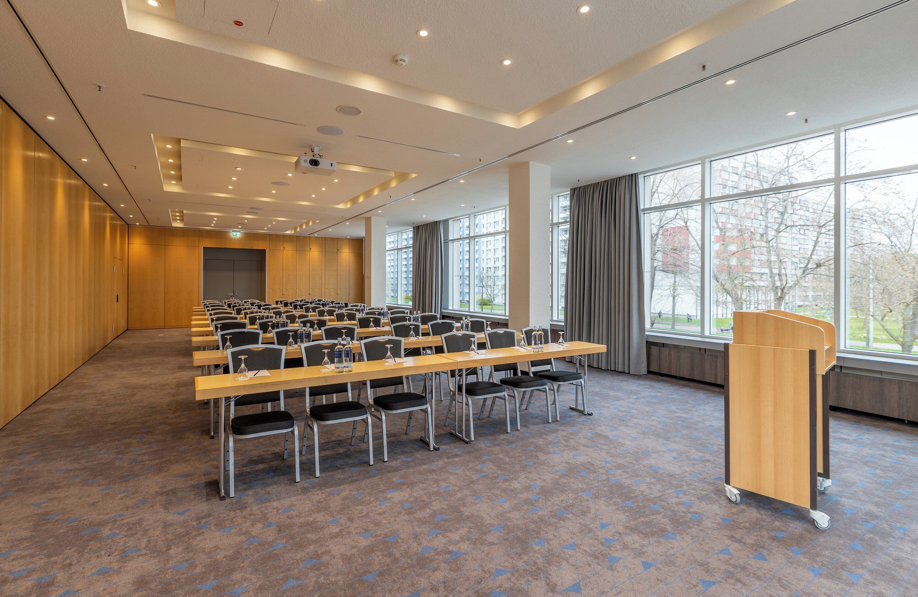 A conference room with rows of chairs, a podium, and large windows.