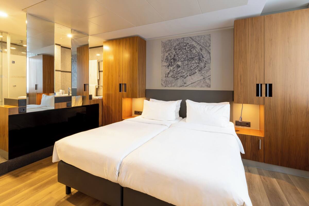 Una habitación de hotel moderna con una cama grande, un armario de madera y un espejo amplio.
