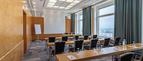 Een vergaderzaal met een lange tafel, meerdere stoelen, een whiteboard en een groot raam met gordijnen.