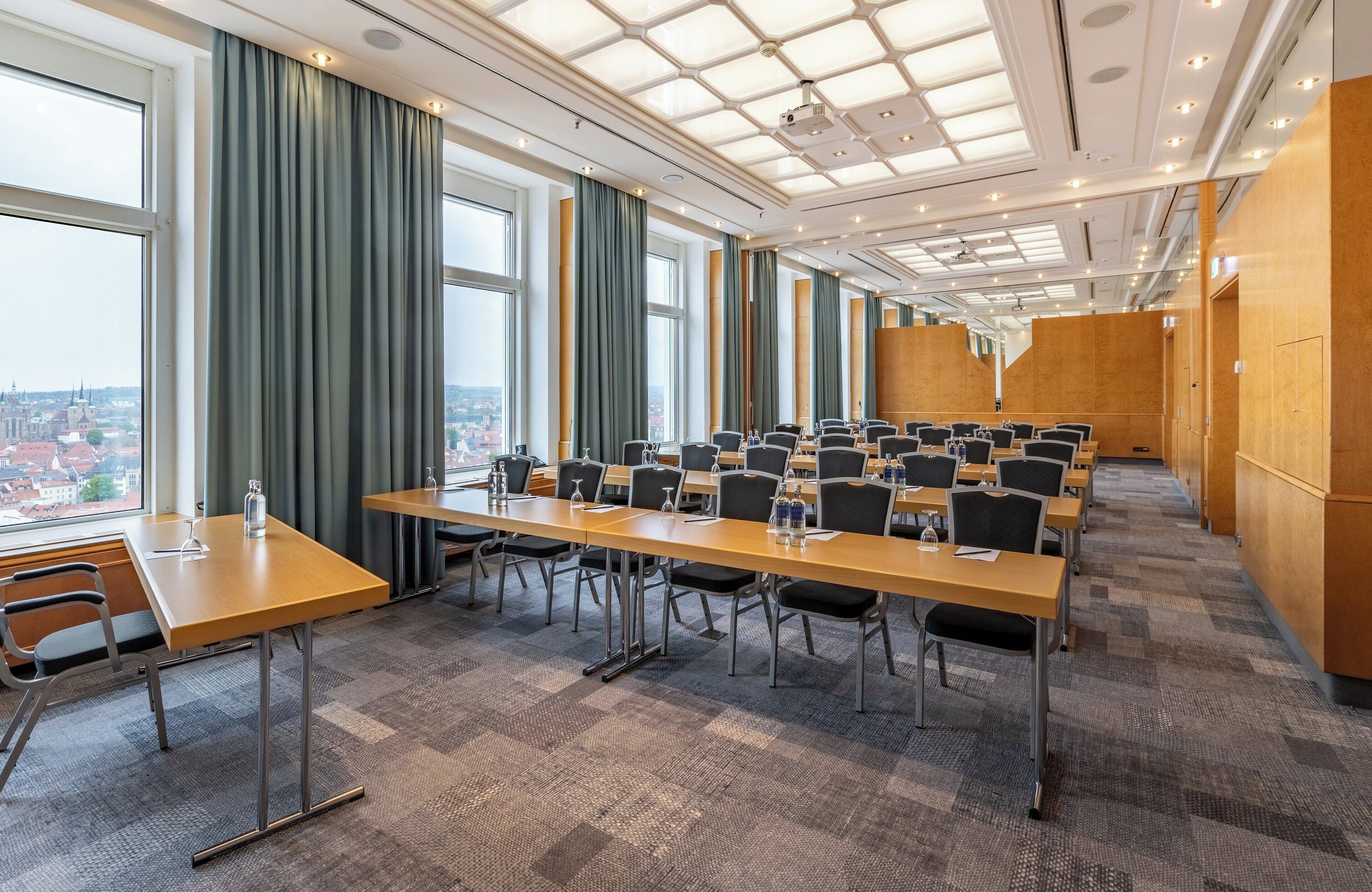 Une salle de conférence dotée de plusieurs tables et chaises, de grandes fenêtres avec des rideaux et offrant une vue sur la ville.