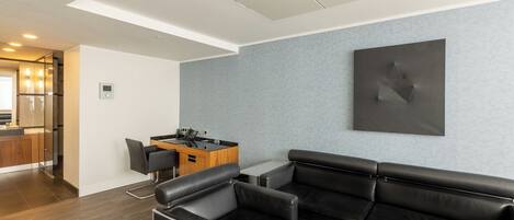 A modern living room with a black leather sofa, a small coffee table, and a kitchen area with a wooden cabinet and a refrigerator.