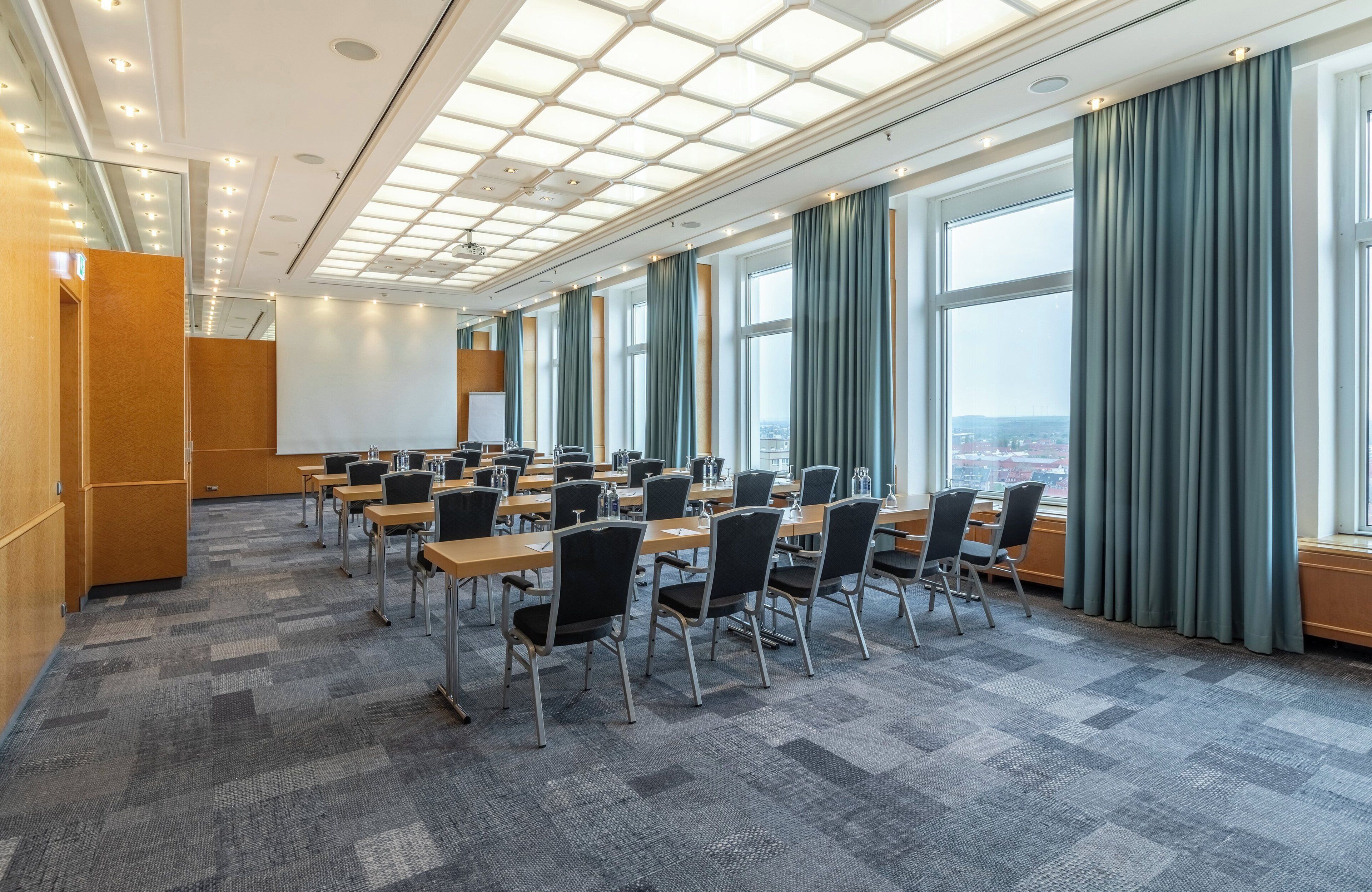 Een vergaderzaal met een hoge plafond, grote ramen en een vloerbedekking.