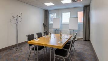 A conference room with a long table, chairs, a coat rack, and windows with curtains.