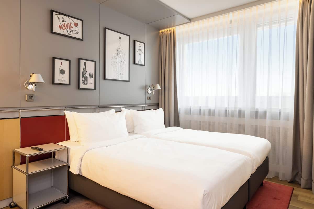 Una habitación de hotel con una cama doble, una mesita de noche con lámpara y cuadros en la pared.