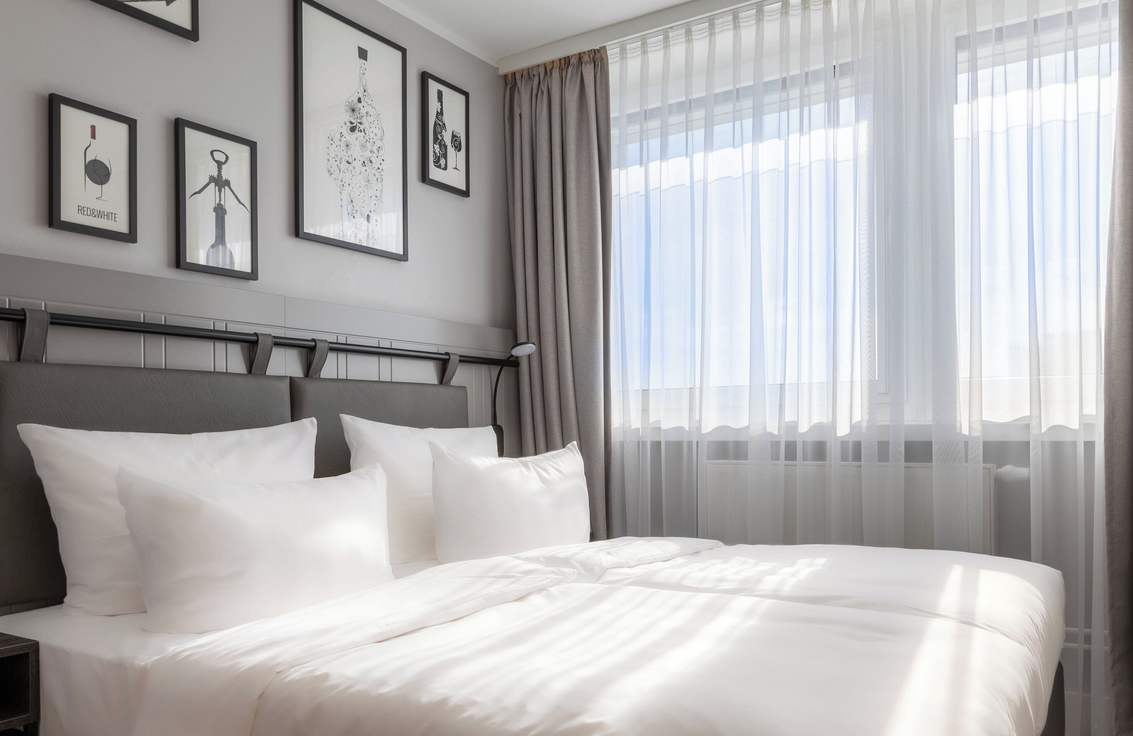 Una cama bien hecha con ropa blanca, un cabecero gris y una mesita de noche con una lámpara.