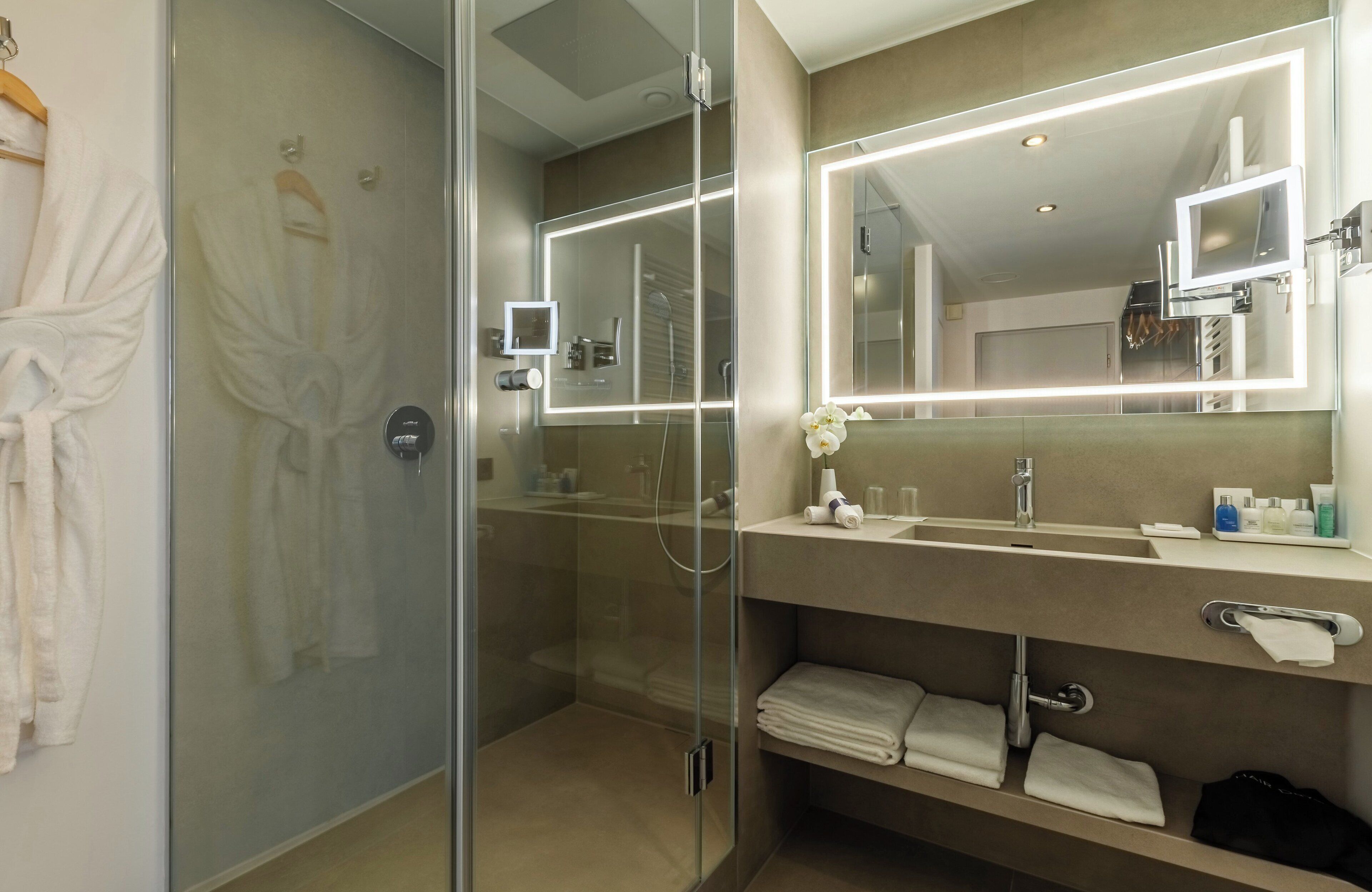 A modern bathroom with a glass-enclosed shower, a large mirror with integrated lighting, a vanity with a sink, and neatly folded towels.
