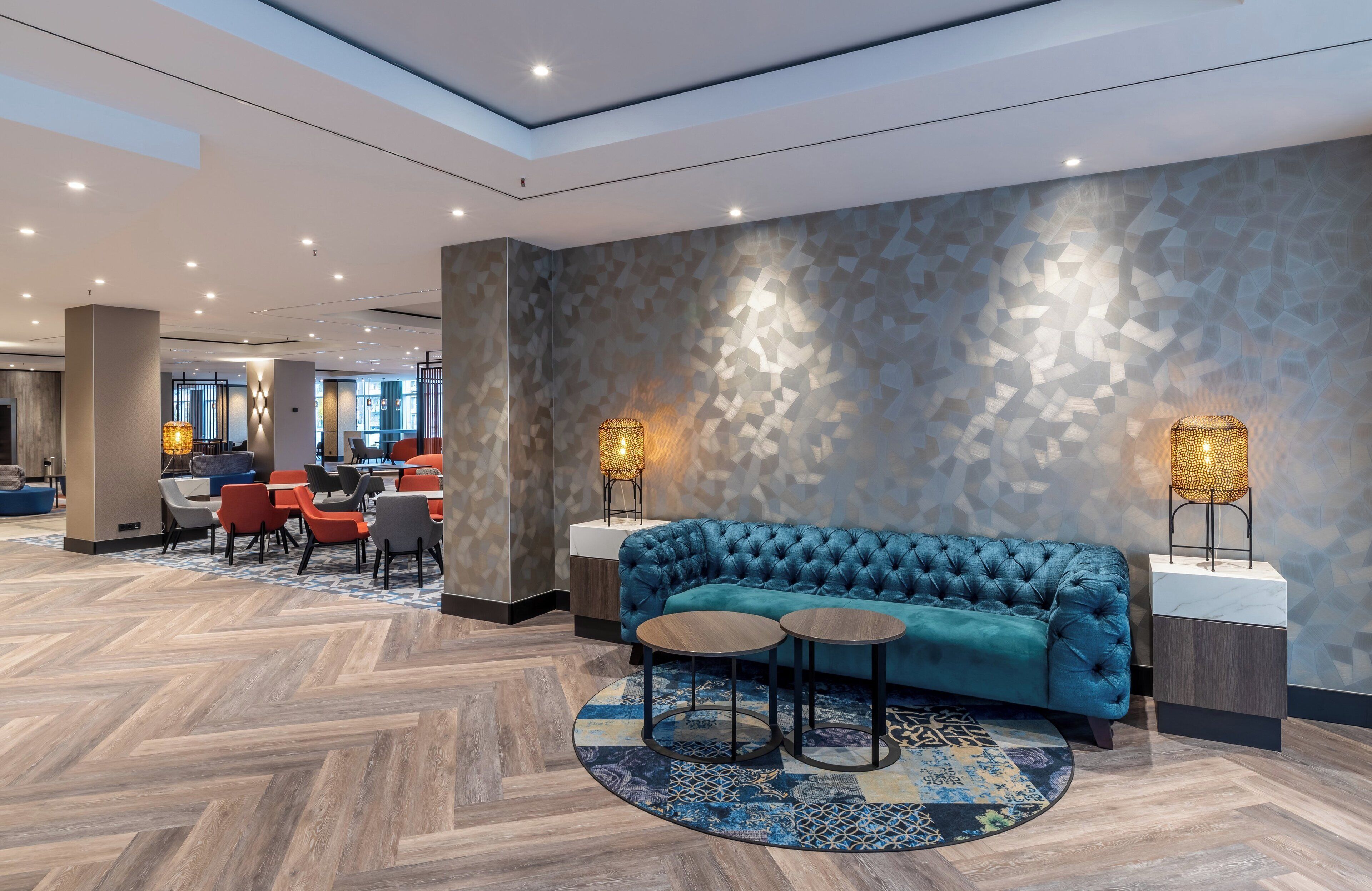 Um lobby moderno com um sofá azul com textura estufada, mesas redondas e um tapete estampado.
