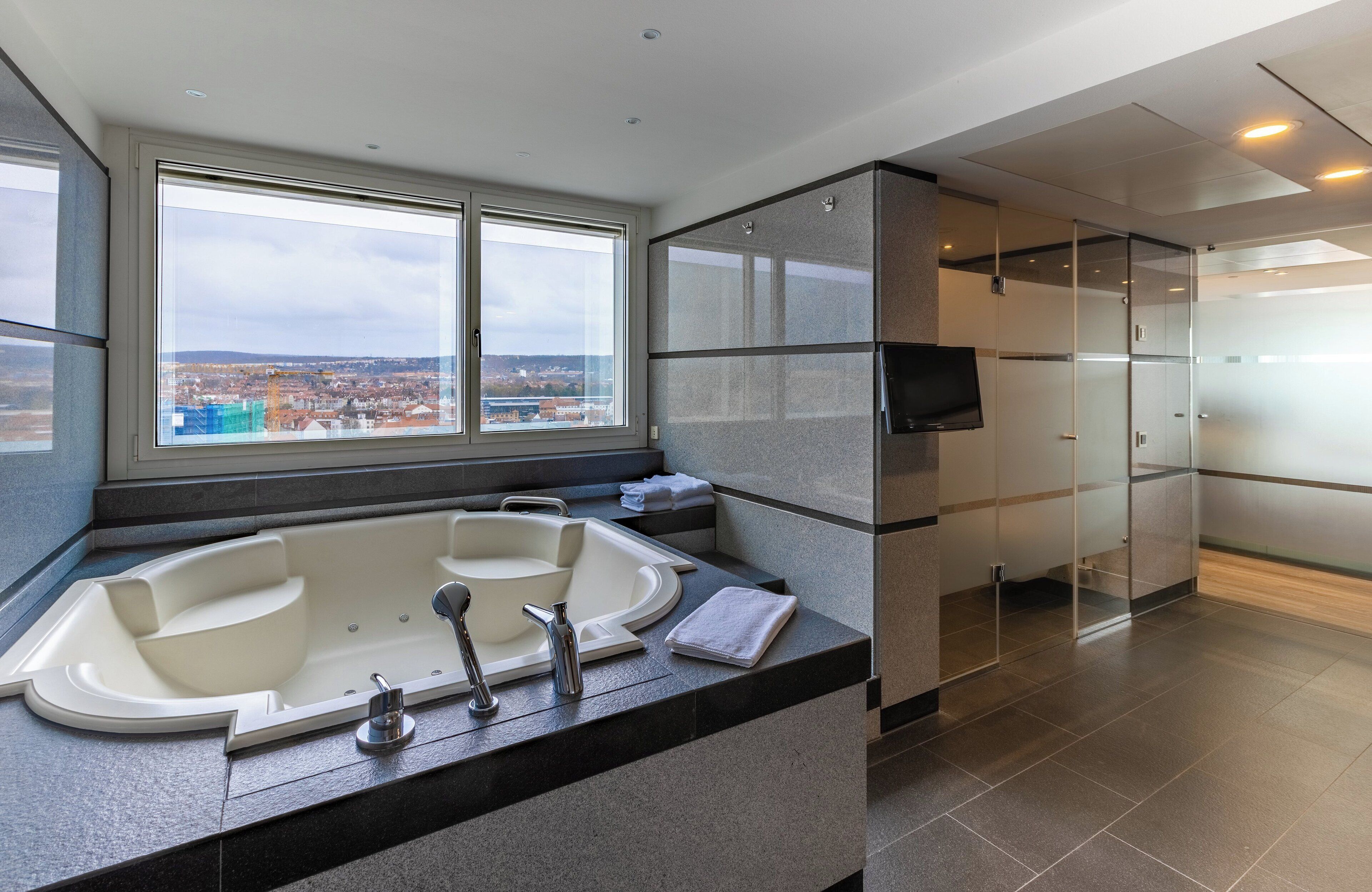 Ein modernes Badezimmer mit einer großen Badewanne, einer Duschkabine aus Glas und Blick auf die Stadt.