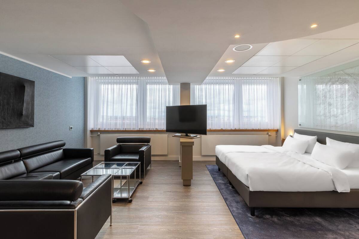 Una habitación de hotel moderna con una cama grande, un sofá, un televisor y un escritorio.