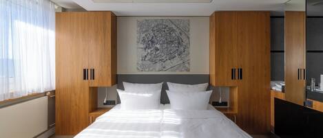 Quarto de hotel moderno com uma cama grande, guarda-roupa de madeira e uma obra de arte com vista para a cidade.