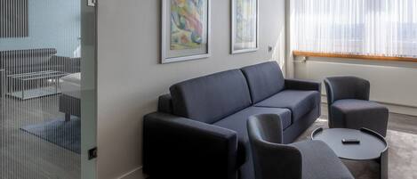A modern living room with a dark sofa, two armchairs, and a small coffee table. There are two framed abstract paintings on the wall.