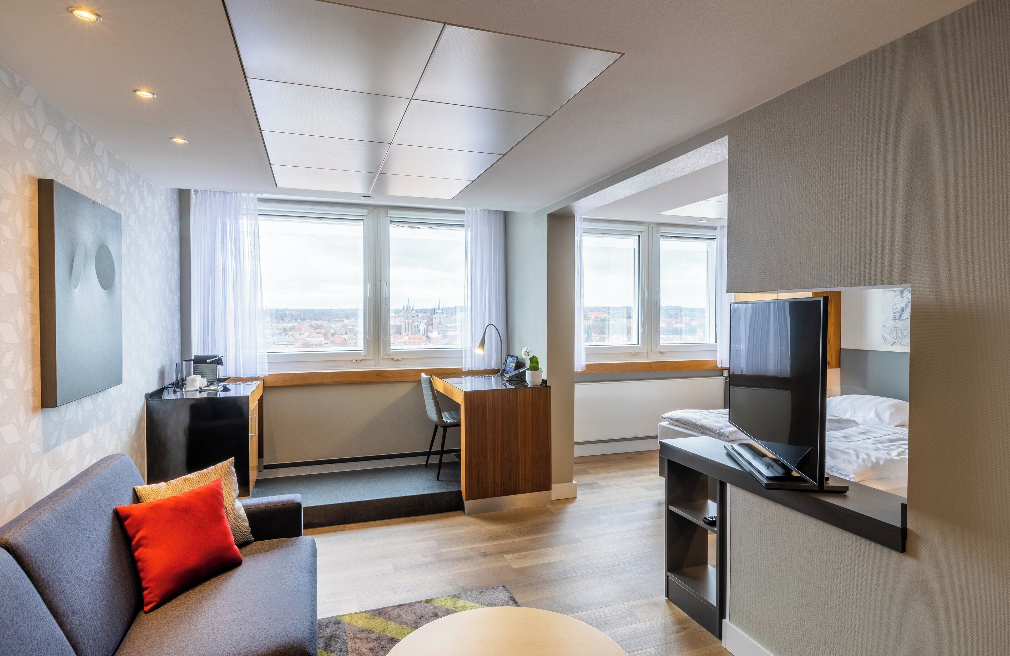 A modern hotel room with a sofa, a desk, a TV, and a bed.