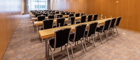 Un salón de conferencias con filas de mesas y sillas, paredes de paneles de madera y suelo alfombrado.