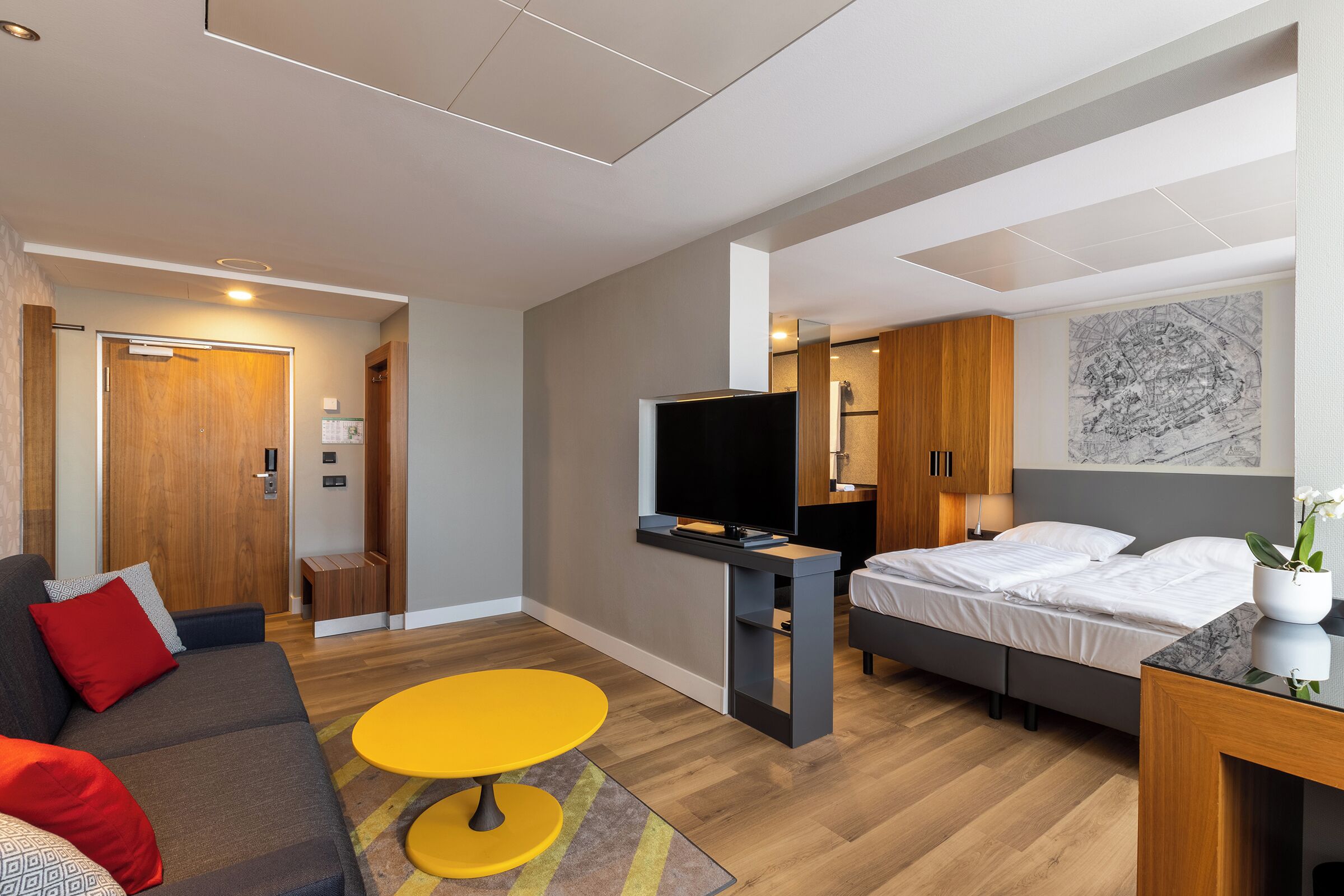 Habitació d'hotel moderna amb un llit, una televisió, un sofà, una taula petita i una porta de fusta.
