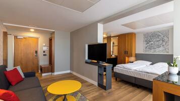 Habitació d'hotel moderna amb un llit, una televisió, un sofà, una taula petita i una porta de fusta.