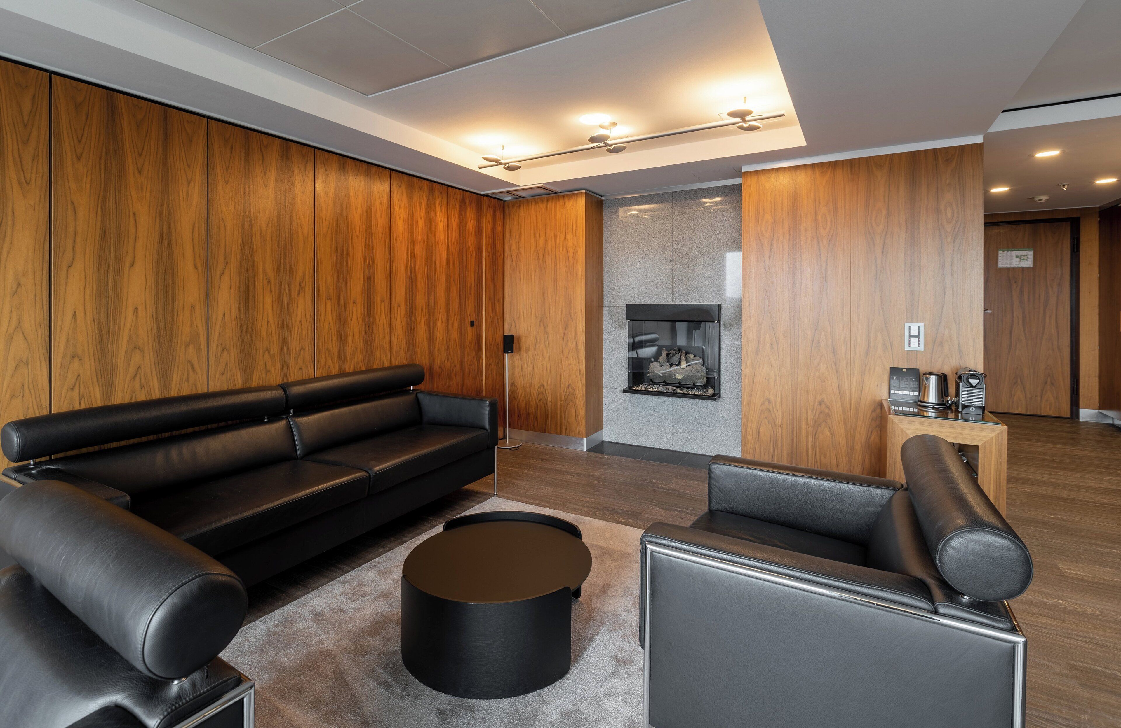 A modern living room with a black leather sofa, a round coffee table, and a fireplace.