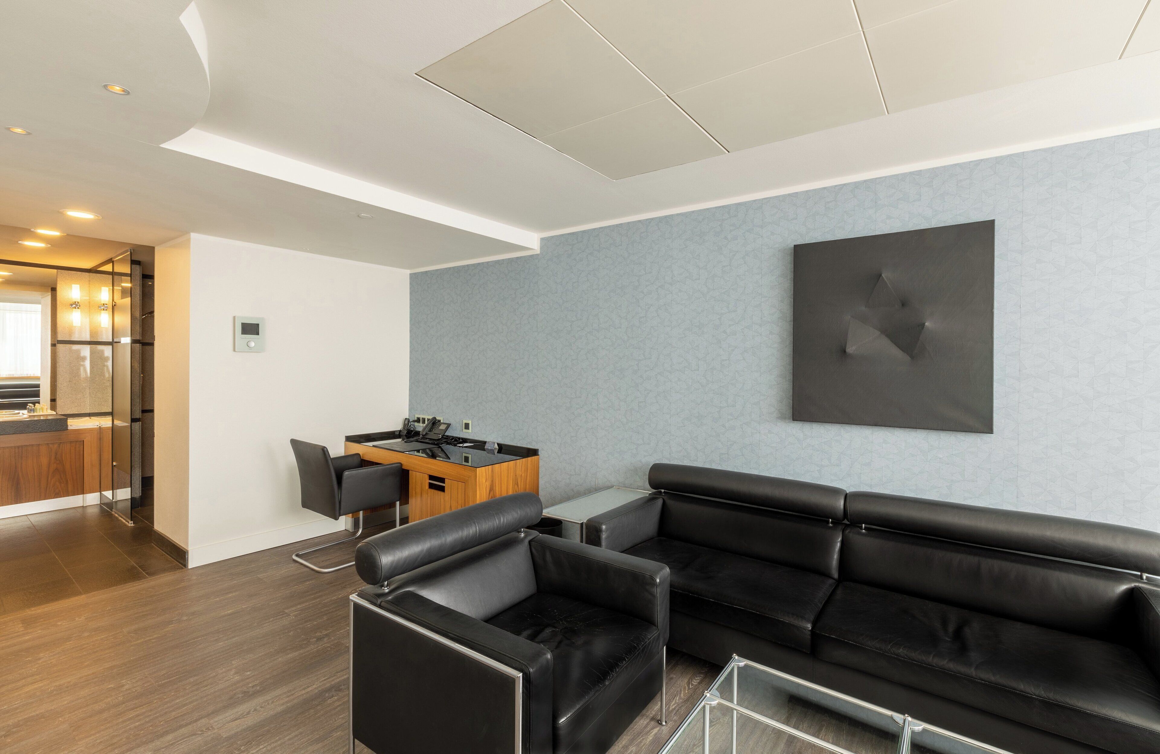 Un salon moderne avec un canapé en cuir noir, une petite table en bois avec des chaises, et un coin cuisine à l’arrière-plan.