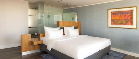 Une chambre moderne avec un grand lit, une table de chevet, une cloison en verre et une œuvre d’art encadrée au mur.