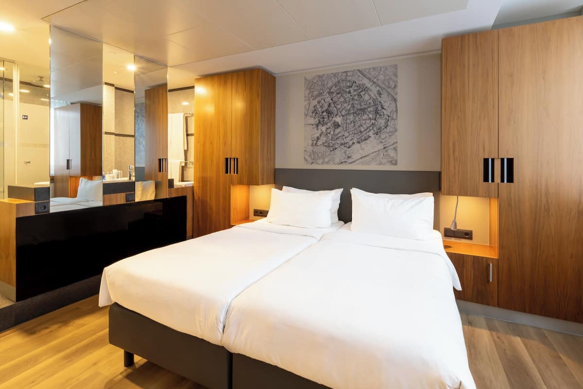 A modern hotel room with a large bed, wooden wardrobe, and a large mirror.