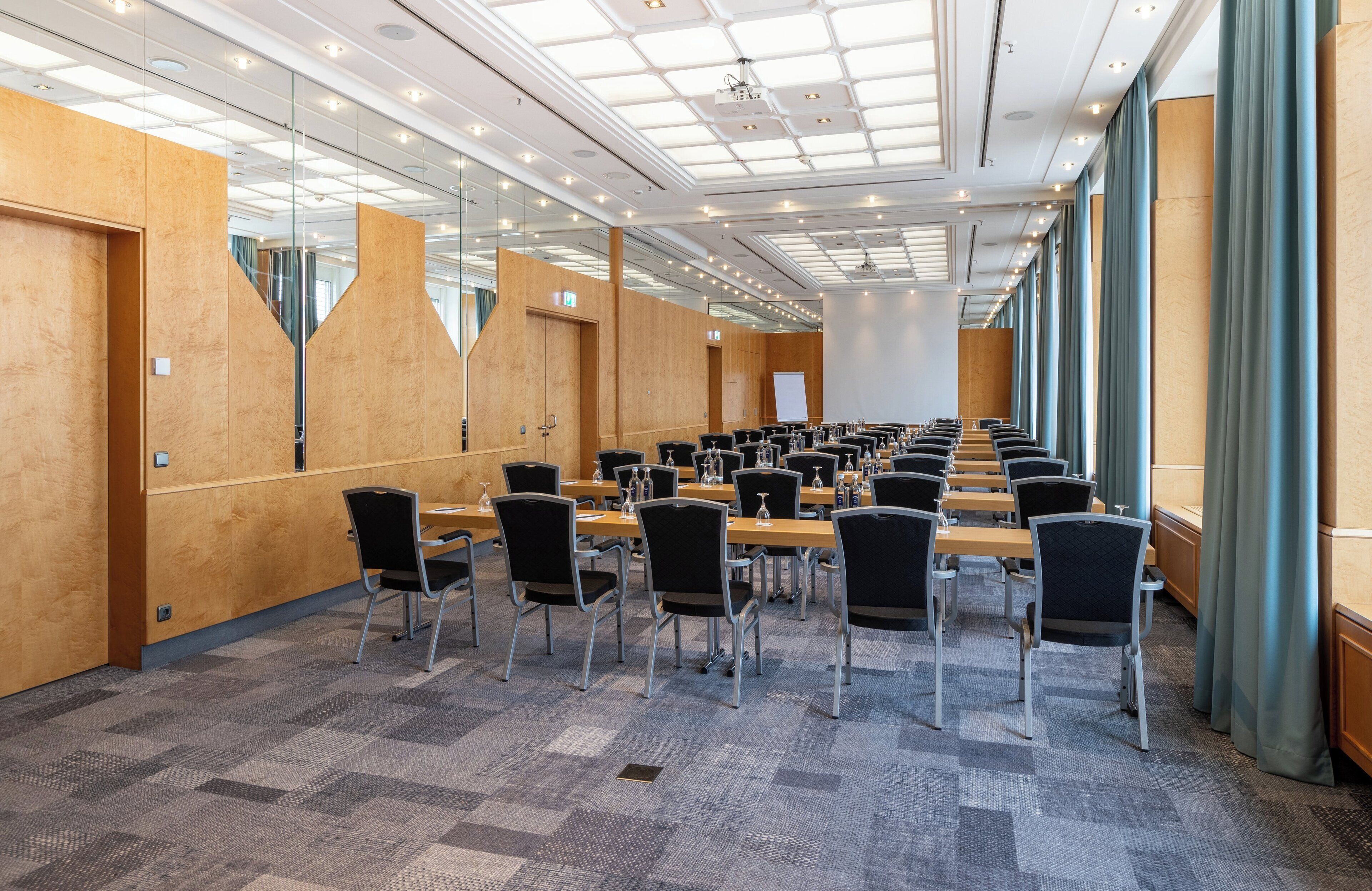 Un salón de conferencias con varias mesas y sillas, amplias ventanas y un diseño moderno en el techo.