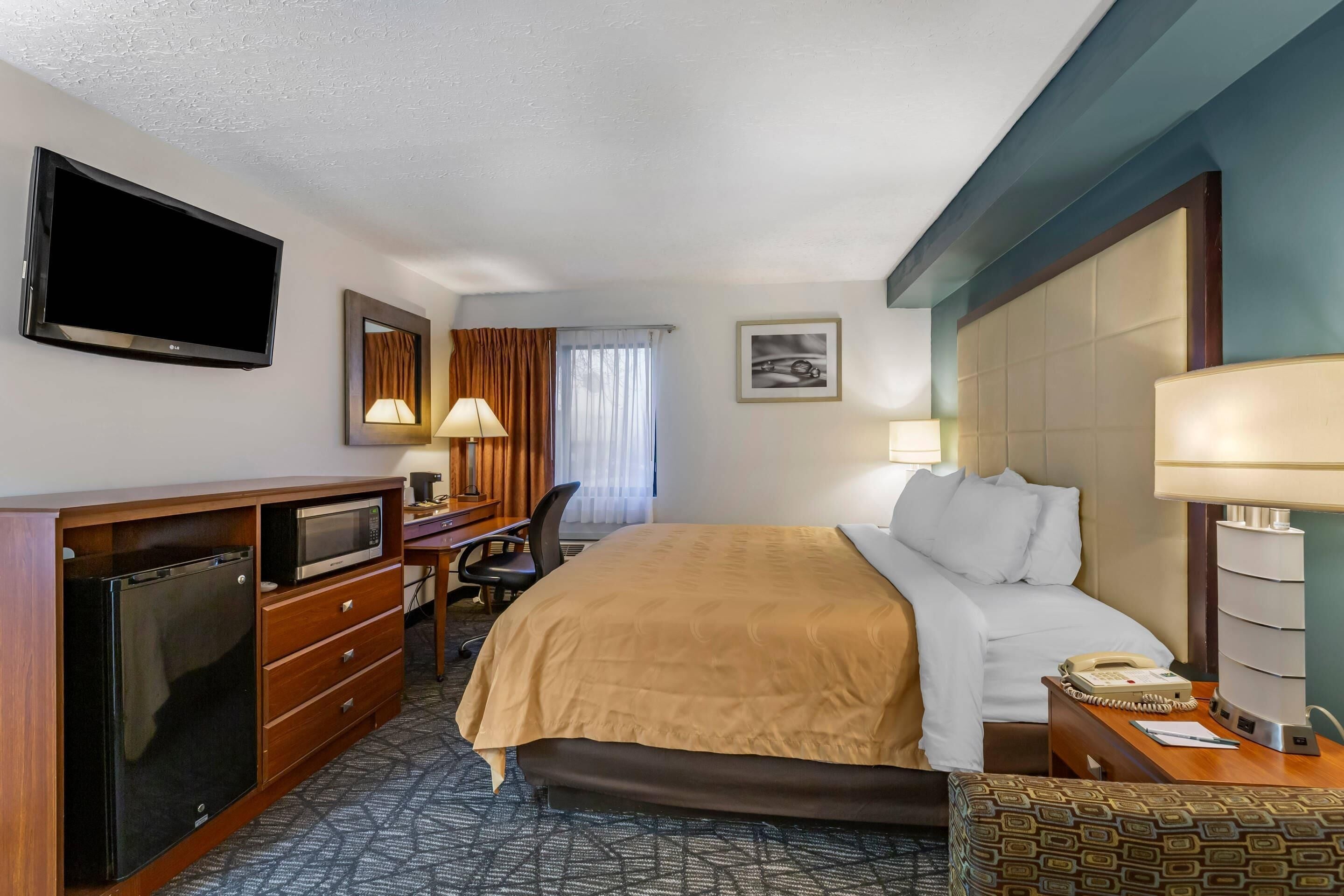 Habitación de hotel con cama, escritorio, silla, televisor y teléfono.