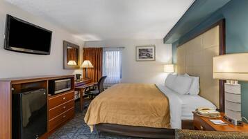 Habitación de hotel con cama, escritorio, silla, televisor y teléfono.