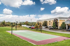 An outdoor tennis court with a net, surrounded by grass and a red border. - Quality Inn Austintown - Youngstown West (Austintown)