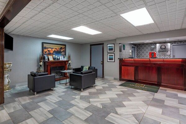 A lobby with a check-in counter, two sofas, a fireplace, and a painting on the wall. - Quality Inn Austintown - Youngstown West (Austintown)