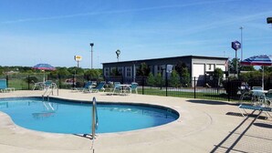 A swimming pool with lounge chairs and umbrellas, a building with a sign, and a fenced area. - Quality Inn Austintown - Youngstown West (Austintown)