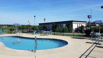 Relax by the clear pool surrounded by lounge chairs and umbrellas, with a building in the background.