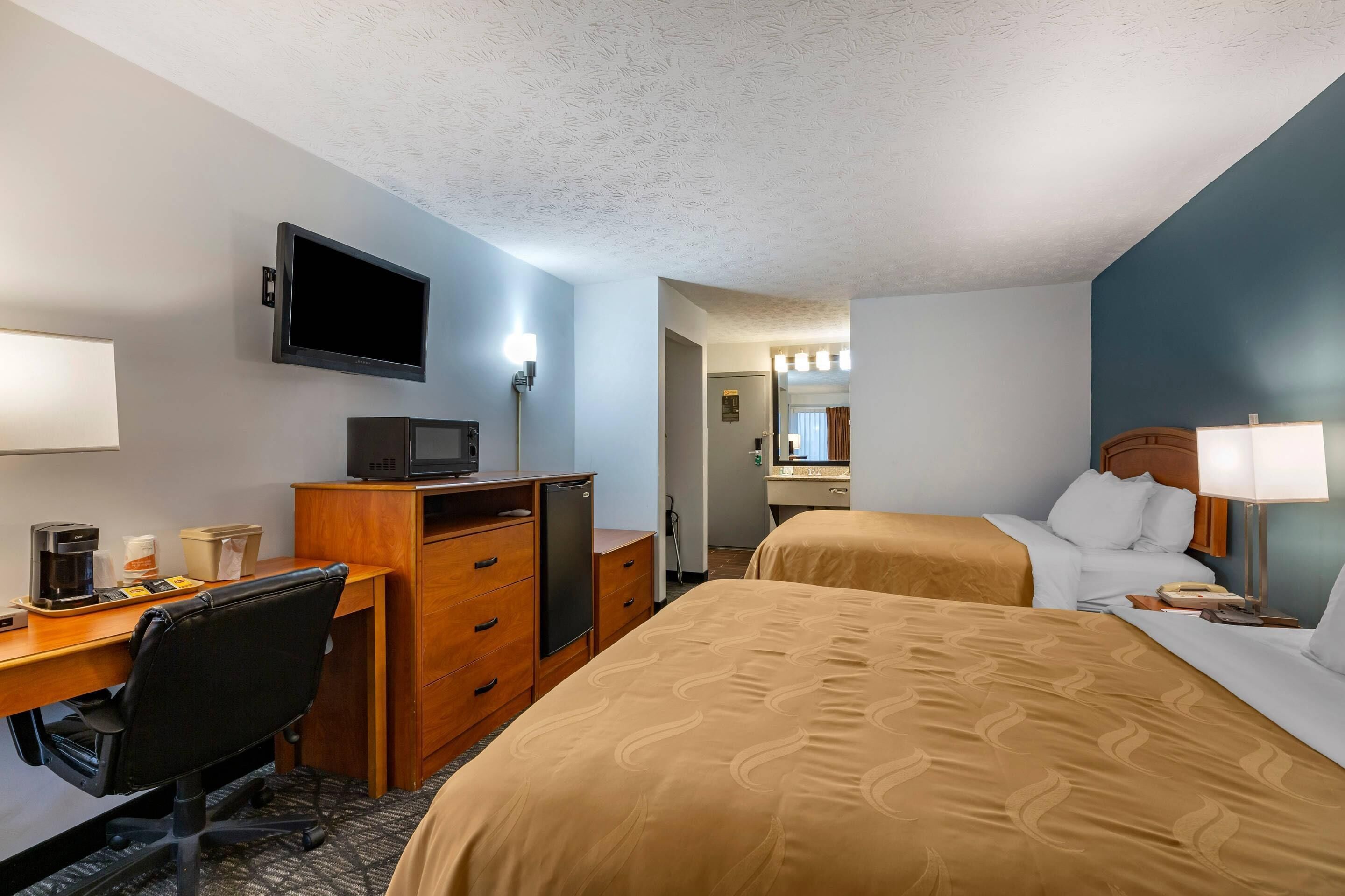 Ein Hotelzimmer mit Bett, Schreibtisch, Stuhl, Fernseher und einer Minibar.