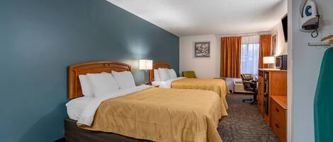 A hotel room with two beds, a desk, a chair, a TV, and a wardrobe.