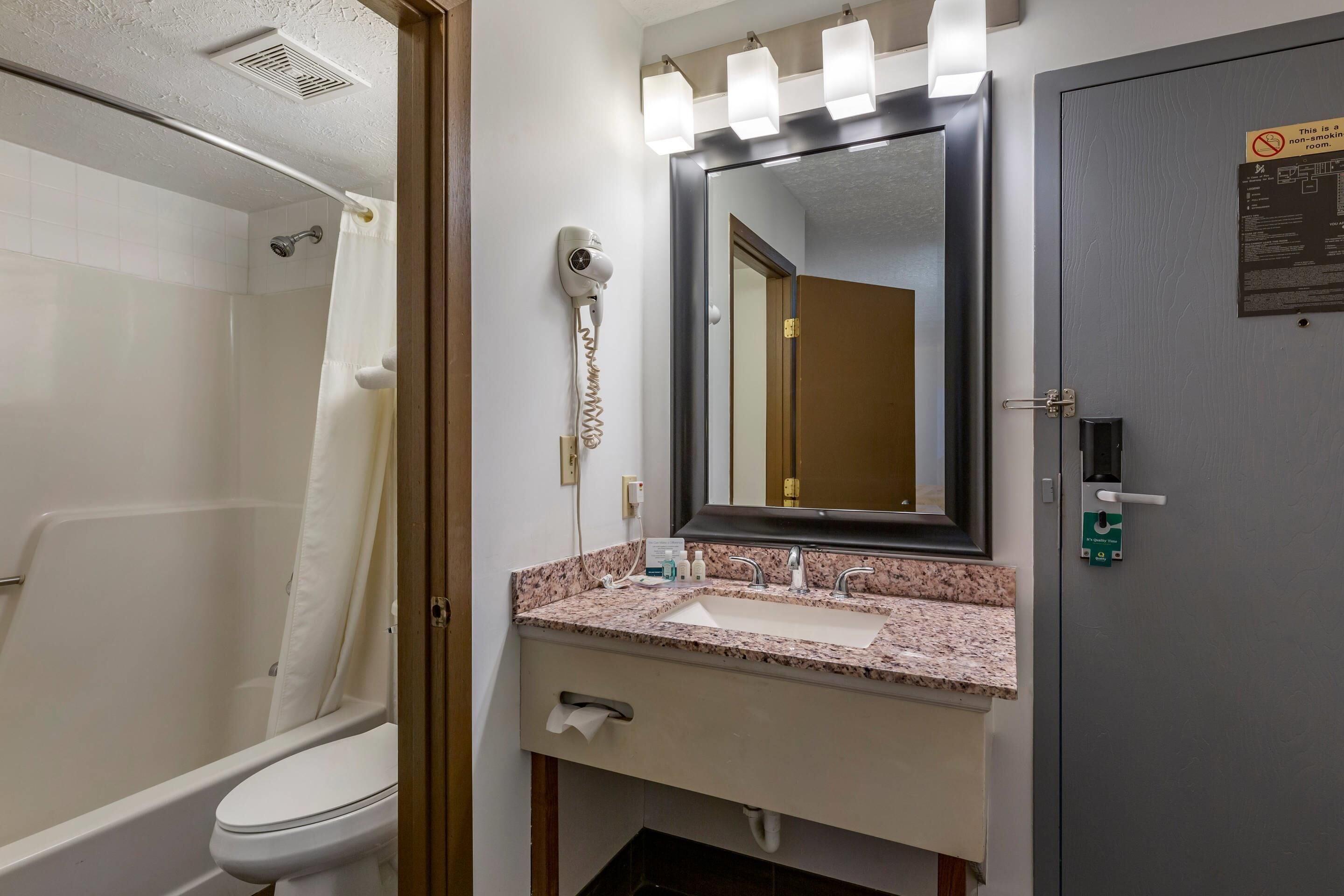 A bathroom with a shower, a toilet, a sink with a mirror, and a hairdryer mounted on the wall.