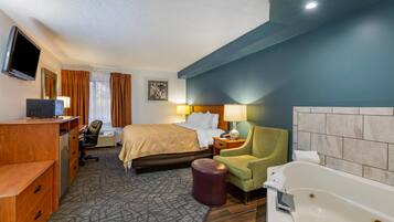 A hotel room with a bed, desk, chair, television, and a bathtub.