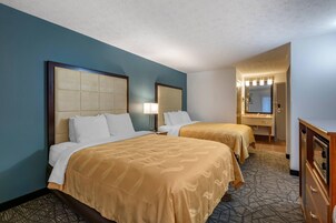 Habitación de hotel con dos camas, un aparador, un espejo y un baño visible a través de una puerta abierta.