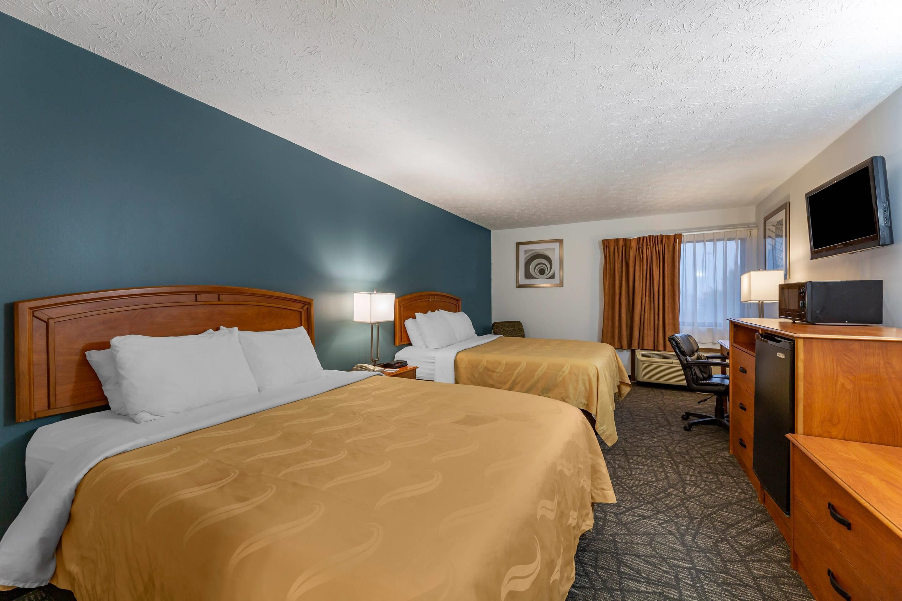 A hotel room with two beds, a desk, a chair, a television, and a picture on the wall.