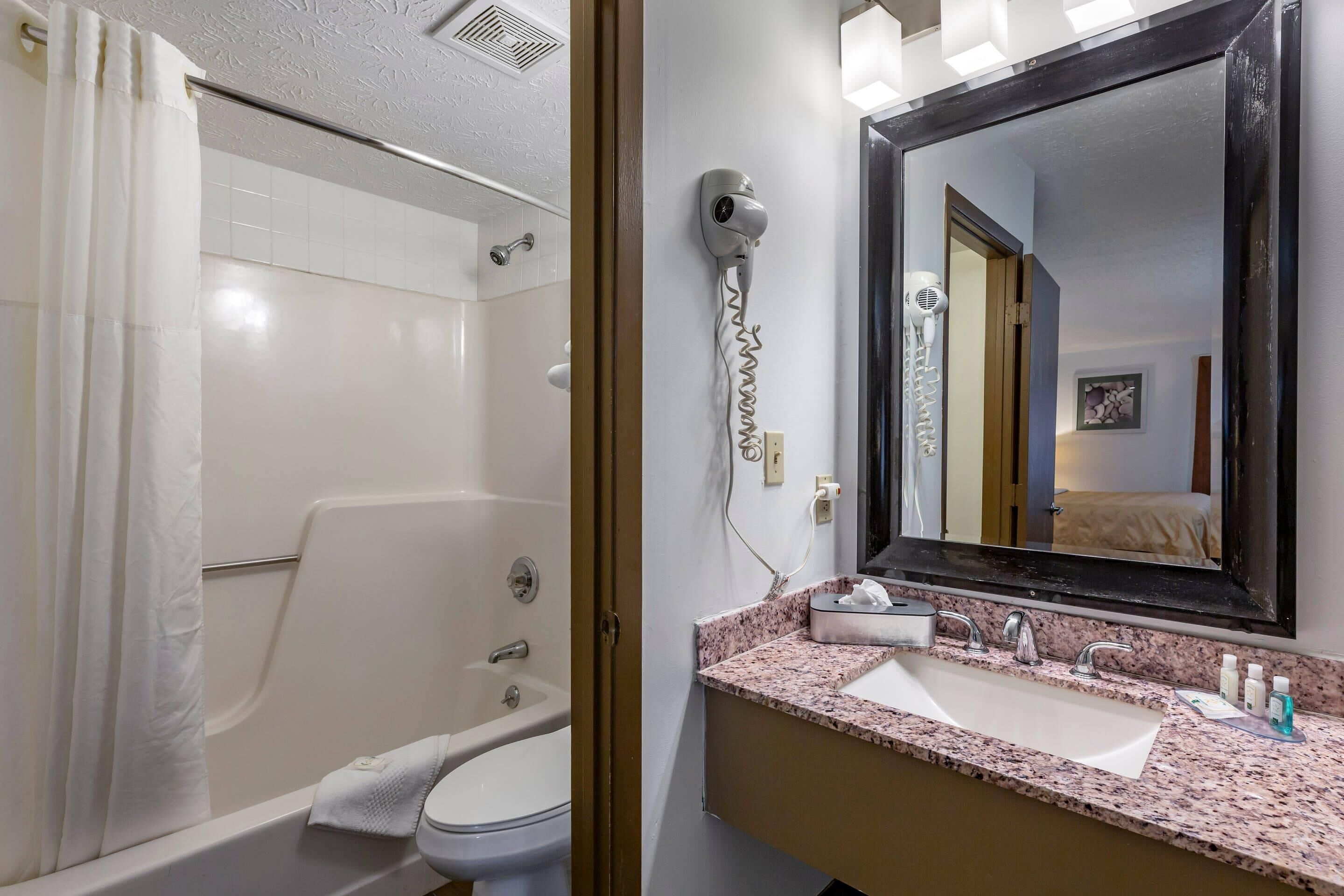 A bathroom with a shower, toilet, sink, and a hairdryer mounted on the wall.