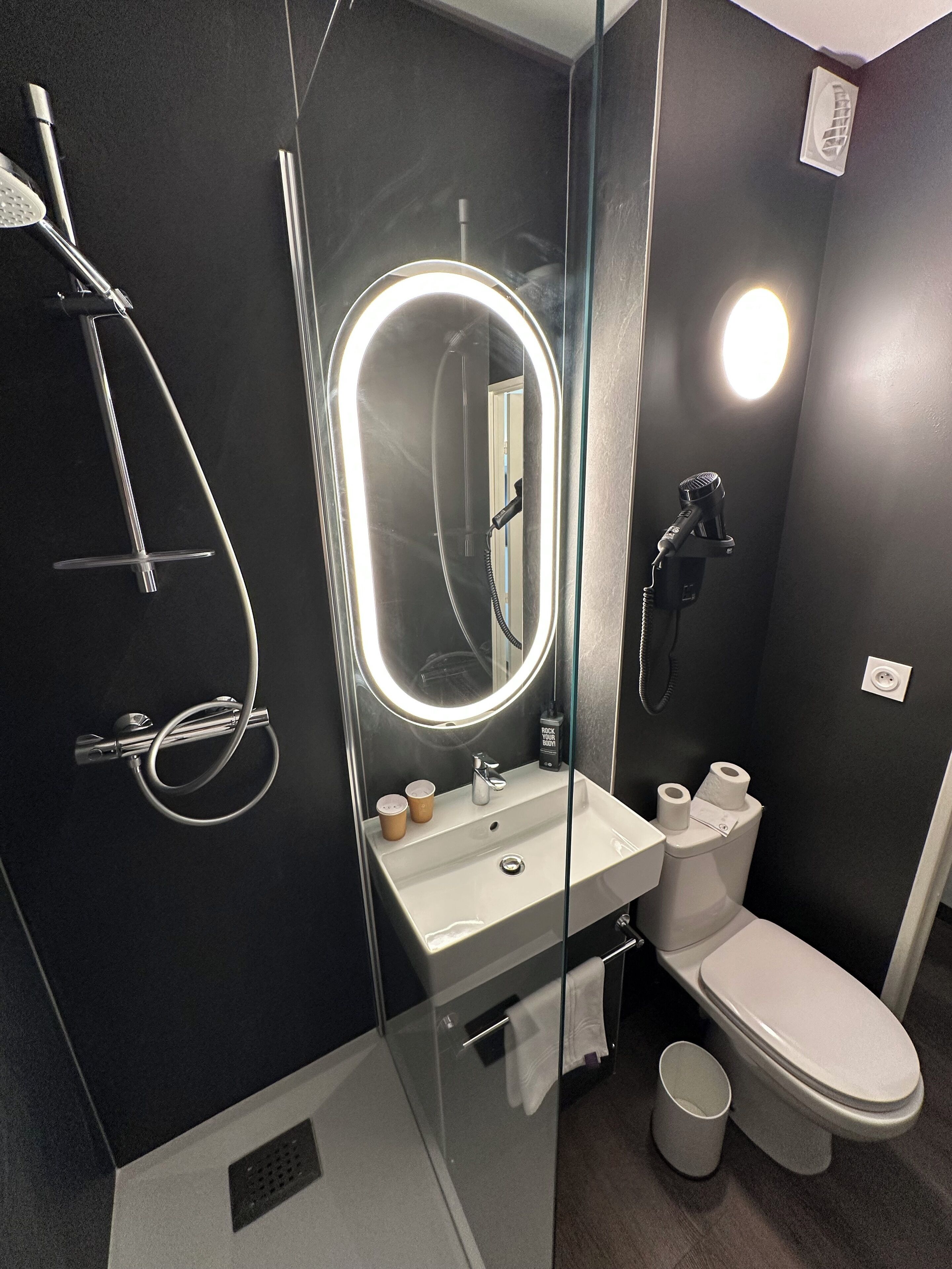 A modern bathroom with a glass-enclosed shower, a white sink with a mirror, and a toilet.
