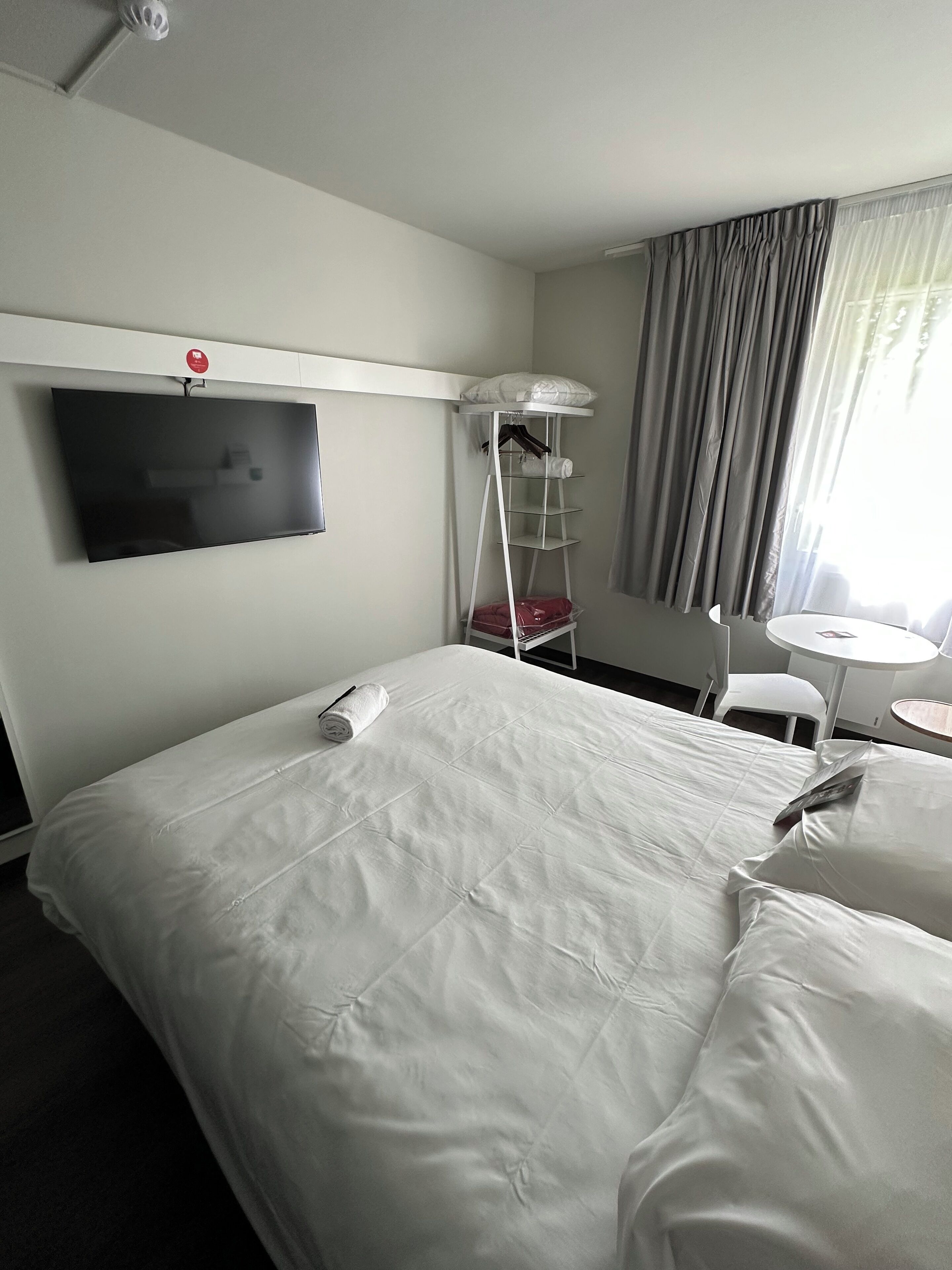 Hotellihuone, jossa on suuri sänky, seinälle asennettu televisio, pieni pöytä ja tuoli.