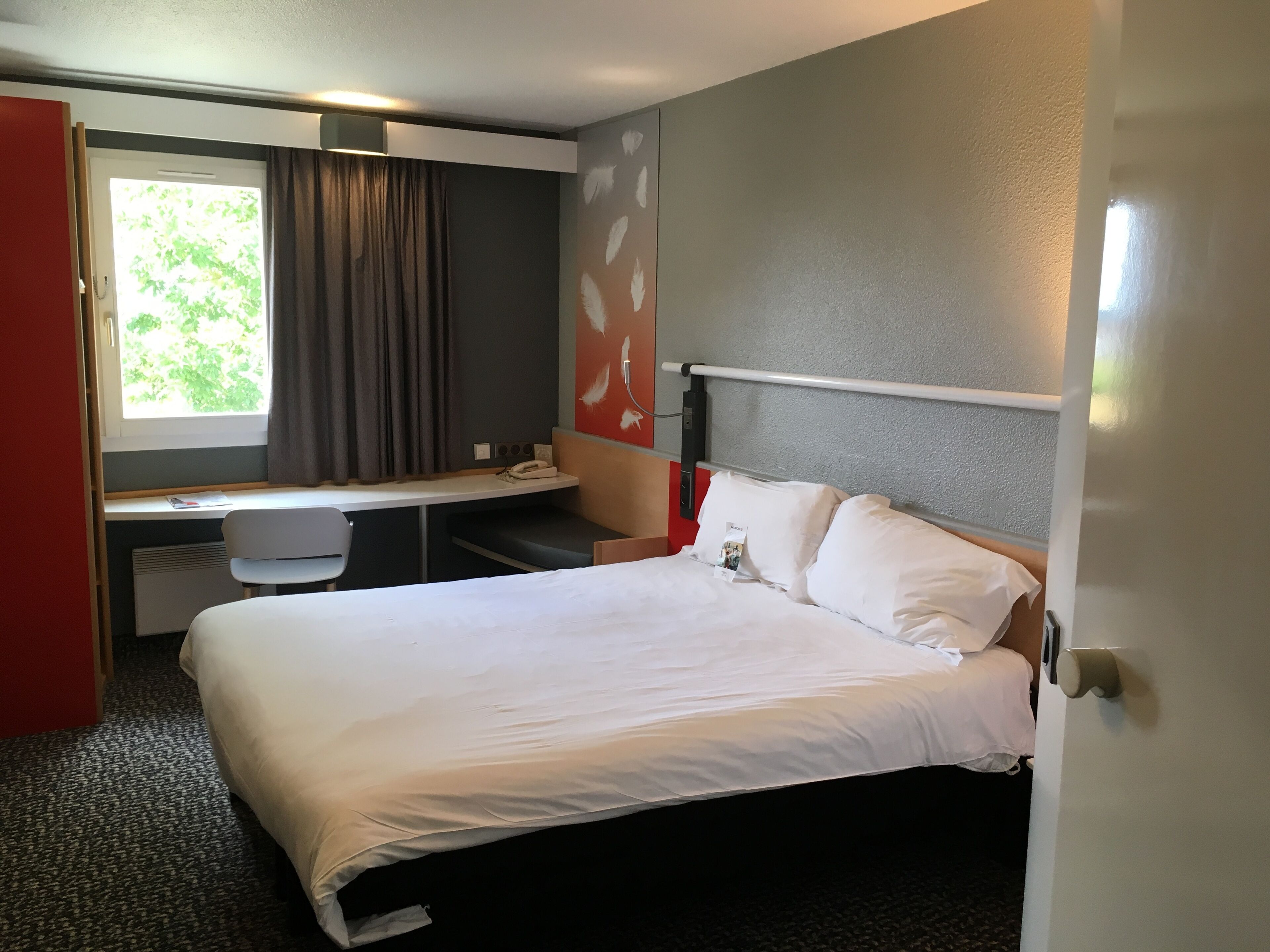 A hotel room with a bed, a desk, and a window with curtains.