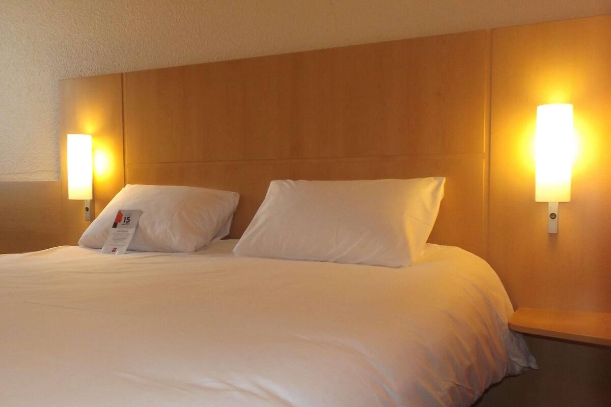Een hotelkamer met een groot bed, twee nachtkastjes en wandlampen.