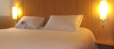 Una habitación de hotel con una cama grande, dos mesitas de noche y lámparas fijadas a la pared.
