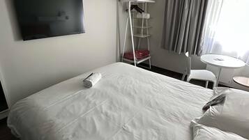 Ein Hotelzimmer mit Bett, Wandfernseher, kleinem Tisch und Stuhl.