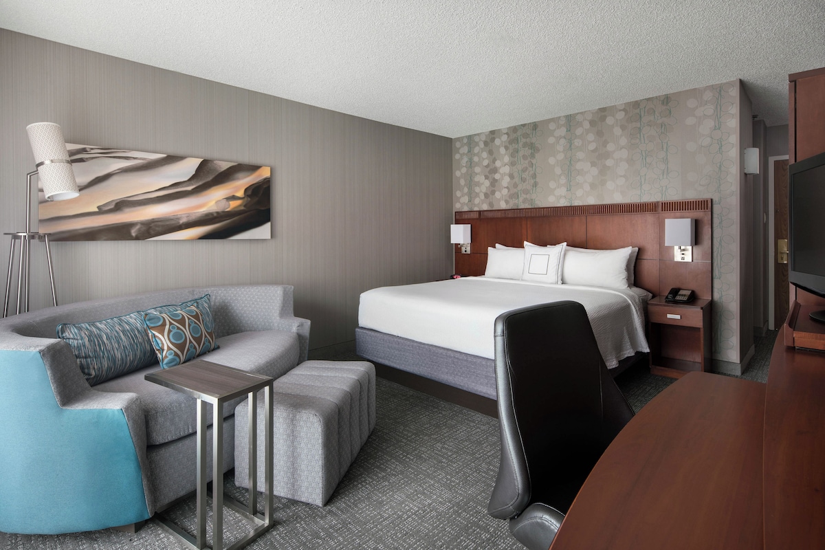 A hotel room with a bed, a desk, a chair, a sofa, and a television.