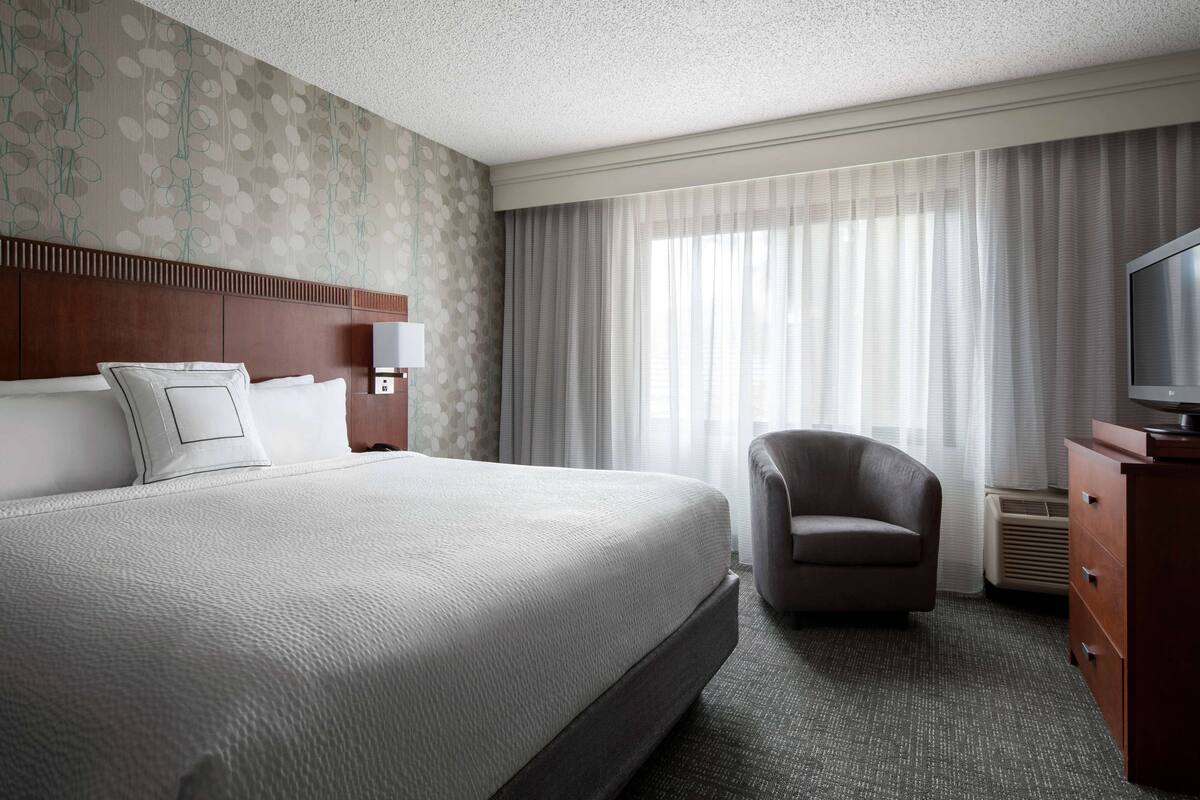 A hotel room with a large bed, a chair, a TV, and a dresser.
