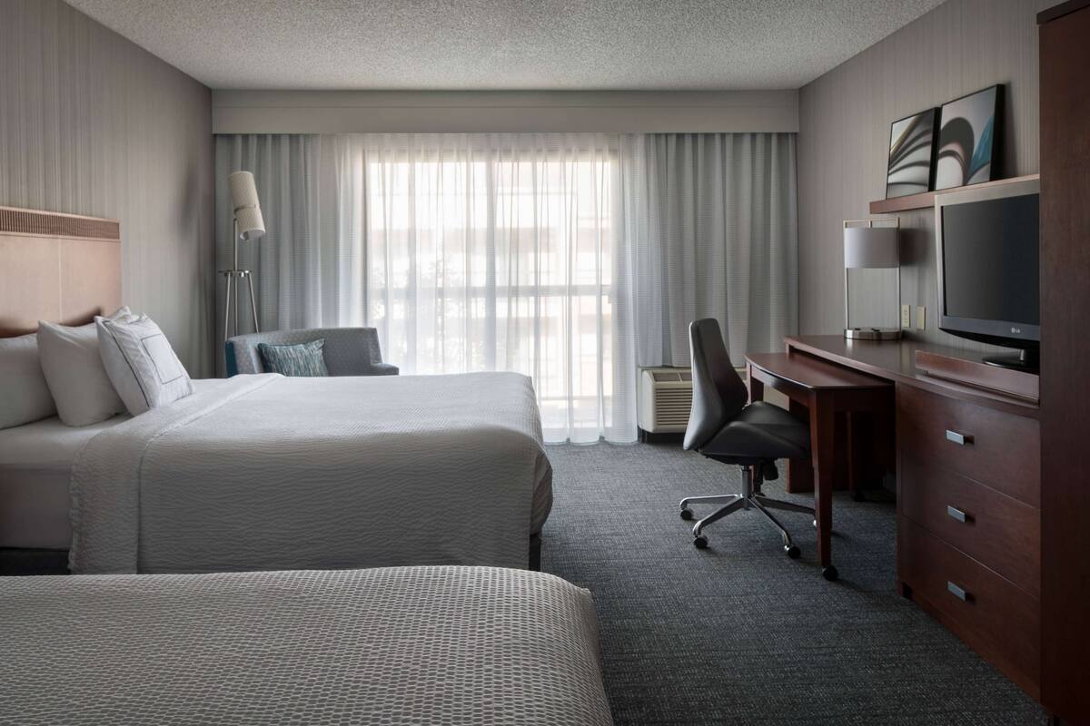 A hotel room with two beds, a desk with a computer, a chair, and a TV.
