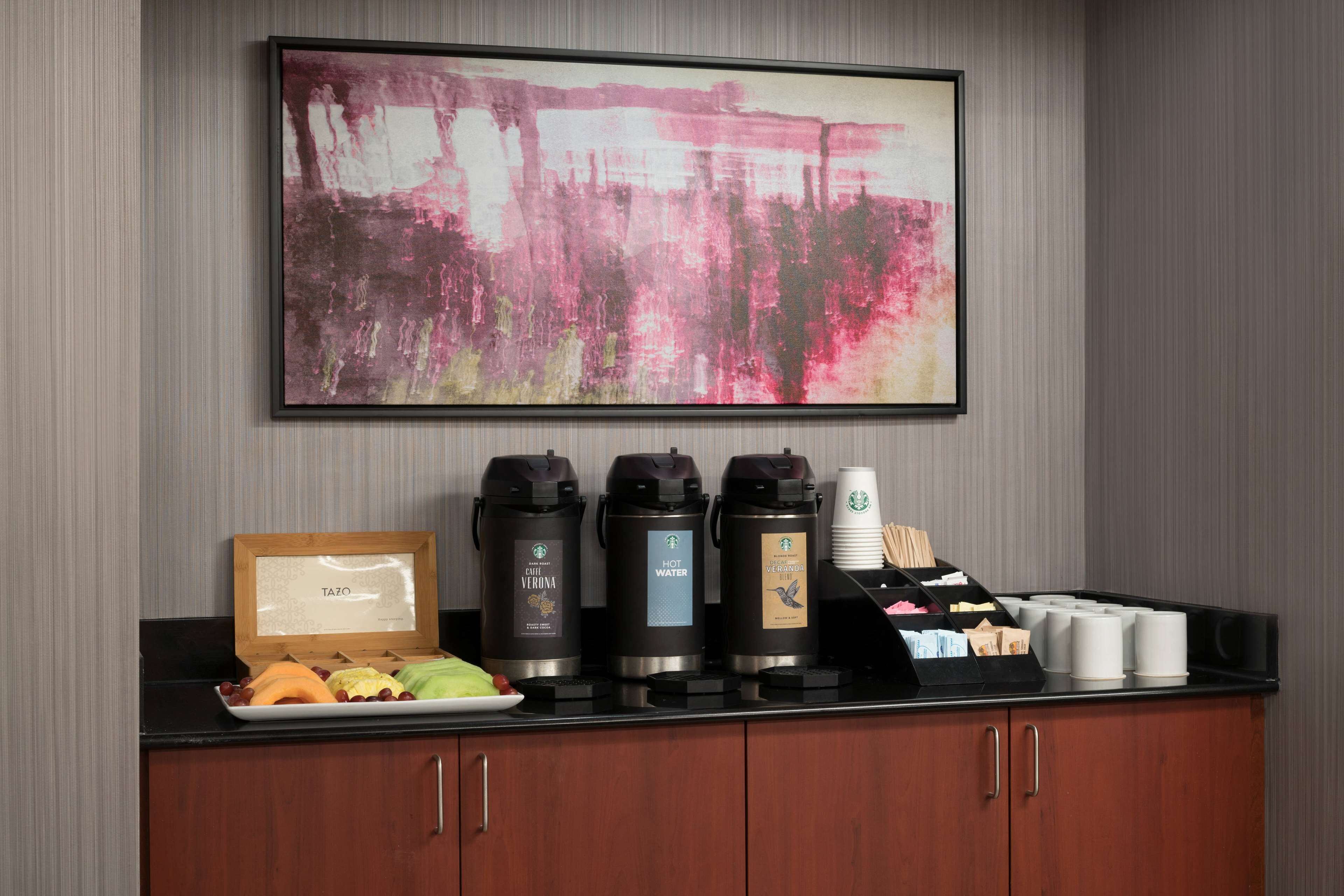 A coffee station with three coffee makers, a tray of snacks, and a framed menu.